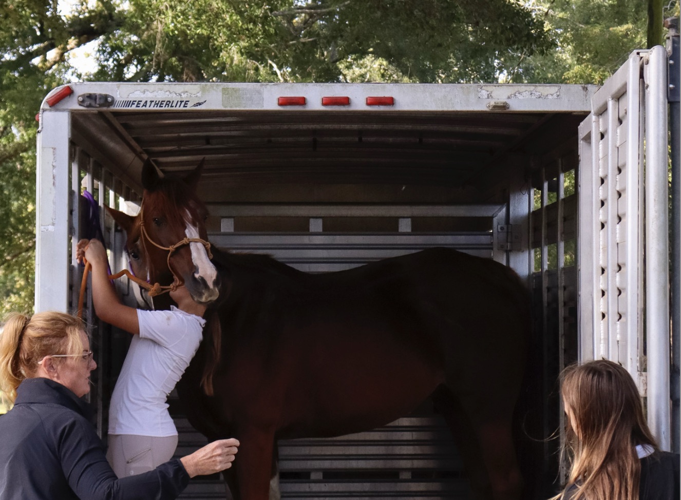 photo of two young girls and farm owner, Lisa Abernathy, loading a horse into a trailer for a show.
